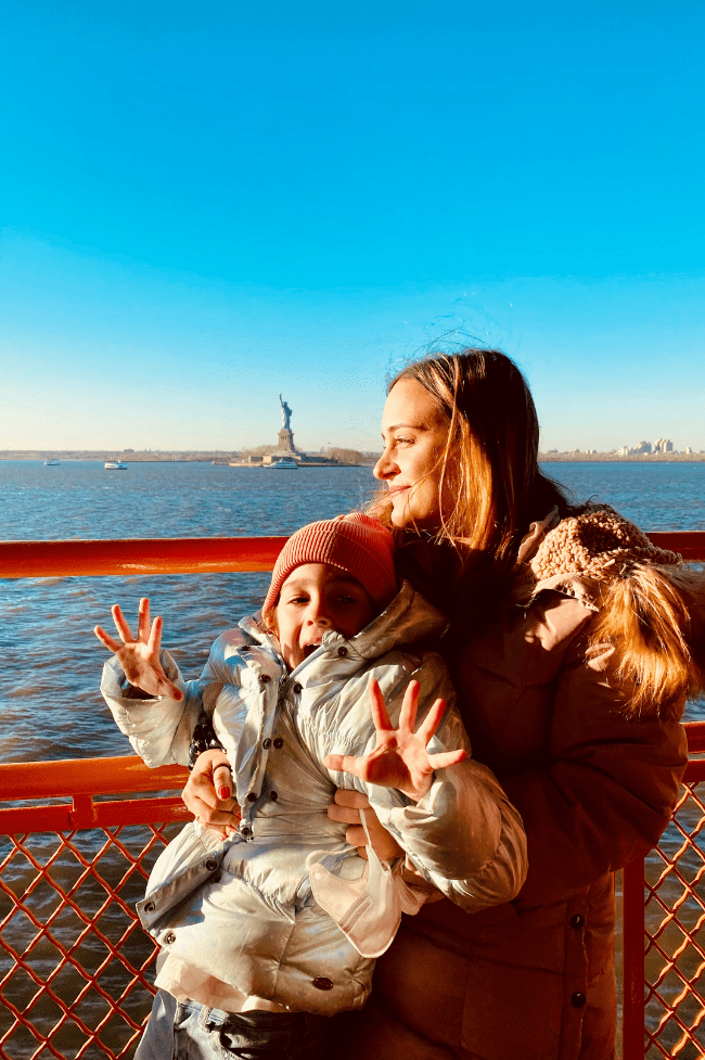 Madre e hija en ferry con la estatua de la libertad atrás