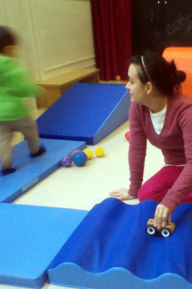 Maestra en el suelo jugando con un alumno Mamá Low-cost